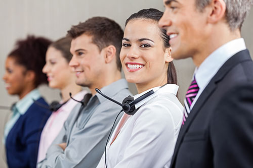 Diverse row of account managers, varied by age, gender and race. Female in the center is looking directly at camera with a smile, satisfied by her team.