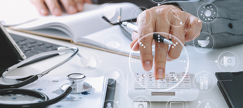 Faceless person at desk with books, laptop, stethescope, calculator.