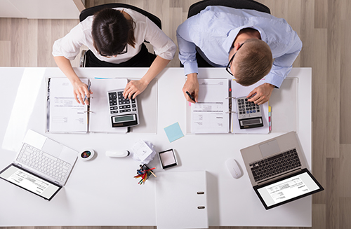 Overhead view of two agents working on a series of calculations and evaluations. We see the top of their heads - close cropped b