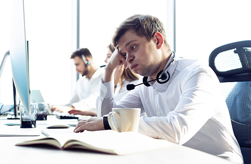 Close up of a young male agent at his text who is feeling frustrated and overwhelmed with no relief in sight.