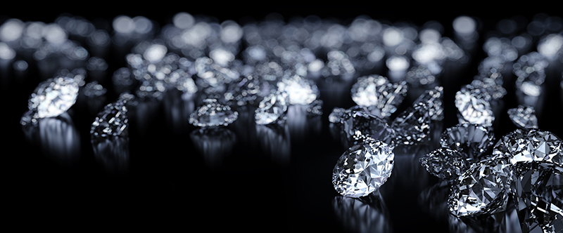 Close up of a handful of jewelry-cut diamonds strewn across a black background.