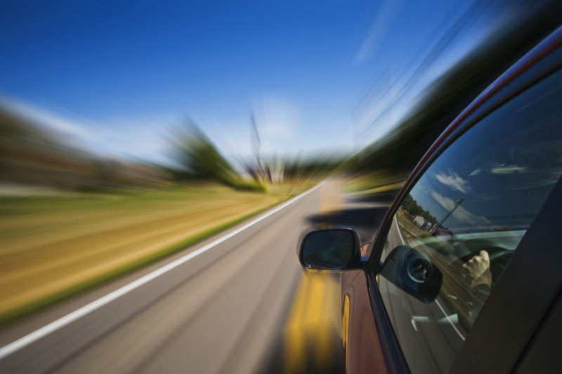 Image shows a car in motion from the viewpoint of the driver hanging their head out the window. Blurred lines indicating motion.