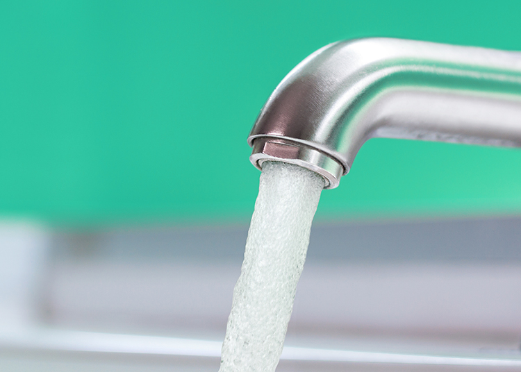 Modern sink faucet running at full force against a sea green background 