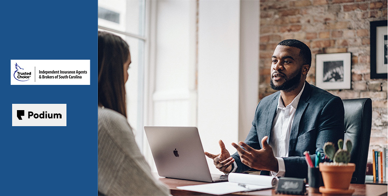 Male agent at his desk consulting with female client in the forground.